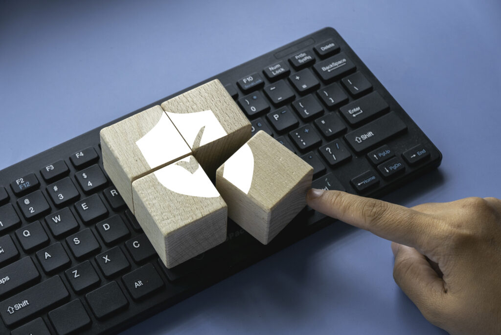 Four wooden blocks rest on a computer keyboard, forming a shield logo with a check mark for strong cybersecurity.