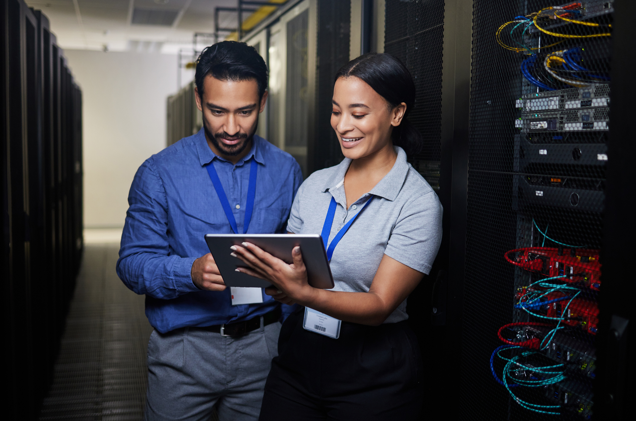 Two IT workers review a gap analysis for CMMC on a tablet while standing in a server room.